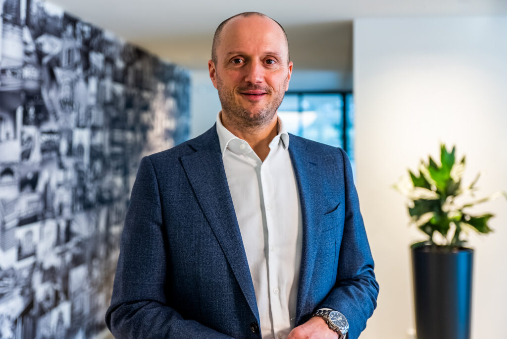 De CEO van Renotec poseert voor een fotowand in een kantooromgeving